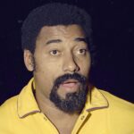 Wilt Chamberlain stands with his mouth open while wearing a yellow Lakers warmup jacket