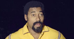 Wilt Chamberlain stands with his mouth open while wearing a yellow Lakers warmup jacket